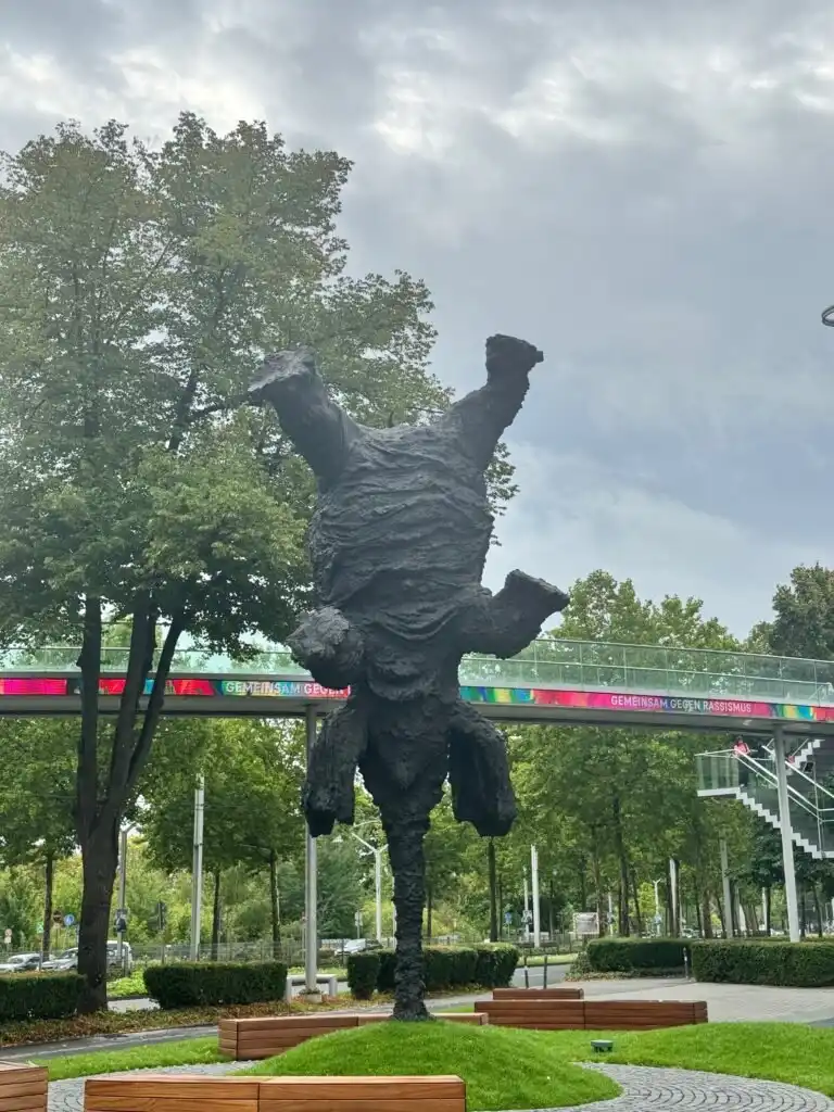 Skulptur im öffentlichen Raum mit Bäumen und einer Brücke im Hintergrund